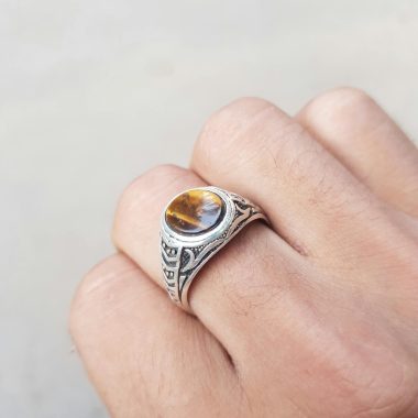 From above hand of crop anonymous person demonstrating silver ring with tiger eye gemstone against white background