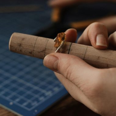 Person Holding a Silver Ring With Gemstone on a Wooden Tube